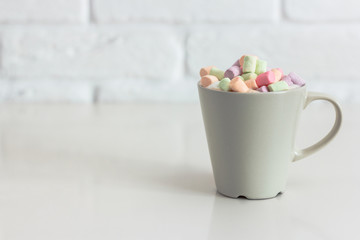 Coffee with multicolored marshmallows and milk in a massive cup on a white brick wall background. Place for a simple text.