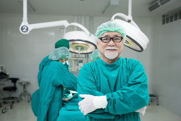 Fototapeta na wymiar Senior male doctor looking to camera with attractive smile at operating room background. Medical concept.