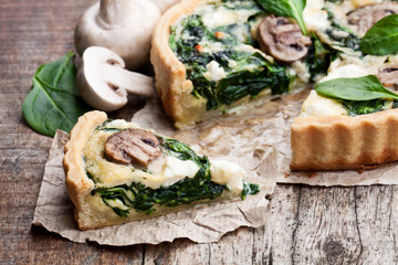 Traditional  french quiche pie with spinach and mushroom on wooden table