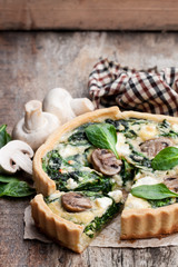 Traditional  french quiche pie with spinach and mushroom on wooden table