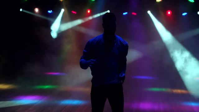 Energetic young man dancing in the dark in a nightclub in the light of bright spotlights in the smoke. Silhouette. Slow motion.