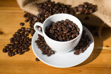 Roast coffee beens in a cup on wooden table.