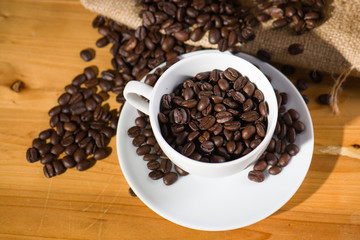 Roast coffee beens in a cup on wooden table.