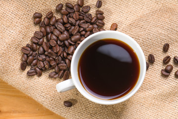 A cup of black coffee with beans on wooden table.