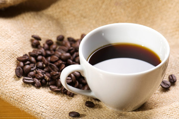 A cup of black coffee with beans on wooden table.
