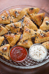 Close-up of meat samosas topped with sesame seeds and served with sauces on a tray, studio shot