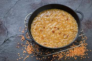 Cast-iron pan with red lentil indian soup or masoor dal on a cracked weathered asphalt background, horizontal shot