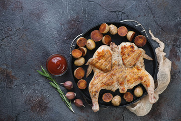 Metal tray with roasted chicken tabaka and cherry potatoes on a weathered asphalt background, horizontal shot with space, top view