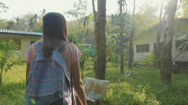 Young woman walking on countryside path through asian village, slow motion.
