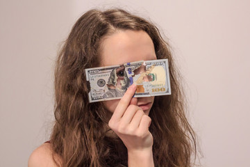 Close-up portrait of mysterious girl looking through the torn dollar banknote