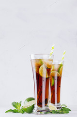 Sparkling summer refreshing cocktail of cola, ice, lime, mint leaf on soft white background with copy space.