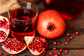 Ripe pomegranates with glass of juice on table