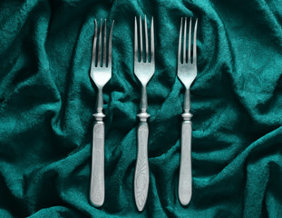 Vintage forks on a green silk tablecloth. Top view.