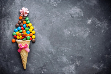 Obraz na płótnie Canvas Ice cream cone with colorful chocolate glaze candy dragee on dark concrete background