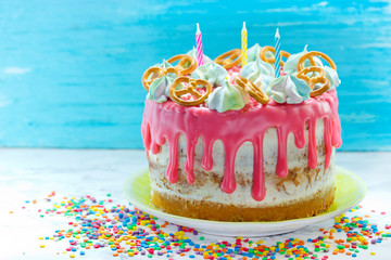 Birthday cake decorated with pink icing, meringue, sprinkle and cookies with candles