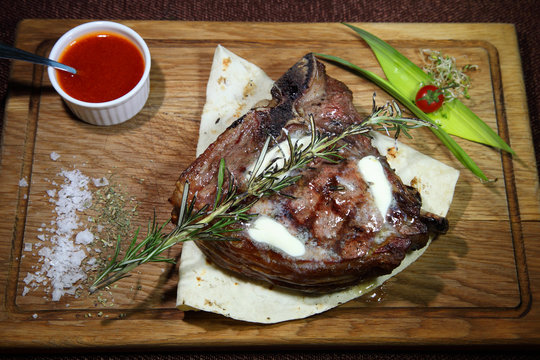 Steak Tibon medium roast on a wooden board with sauce and salt.