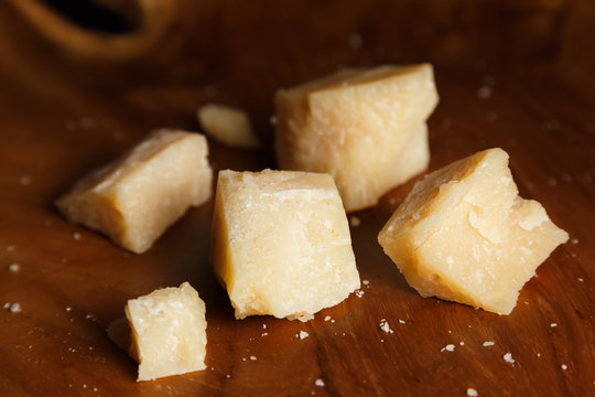 Pieces of parmesan or parmigiano reggiano cheese on a wooden board. Parmesan cheese uses in pasta, risotto and salads. Close-up.