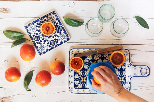 Woman's hand preparing blood orange juice over white wooden table