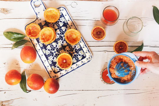 Woman's hand preparing blood orange juice over white wooden table