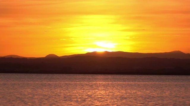 Sunset timelapse in Albufera, Valencia, natural landscape. Long shot at dusk over mountains behind lake red and oranges warm colors