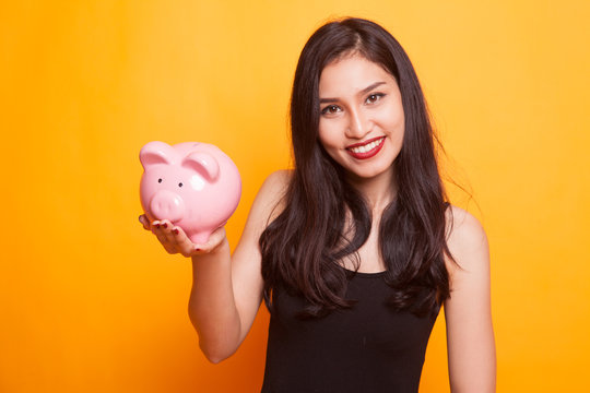 Asian woman thumbs up with pig coin bank.
