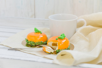Bright orange mousse cakes and cup of coffee on white wooden tray