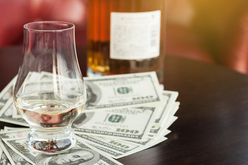Exclusive Scott and Japanese whisky with dollars bank notes on wooden table in luxury bar, tip for good service.  Film tones conception.