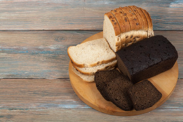 Many mixed breads and rolls of baked bread on wooden table background.