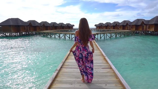Female going on bridge on beach with transparent water of ocean in Maldives