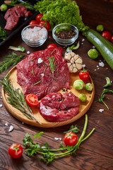 Still life of raw beef meat with vegetables on wooden plate over white background, top view, selective focus
