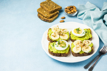 Obraz na płótnie Canvas Healthy breakfast toasts with avocado, eggs, banana and nuts. Selective focus, space for text.