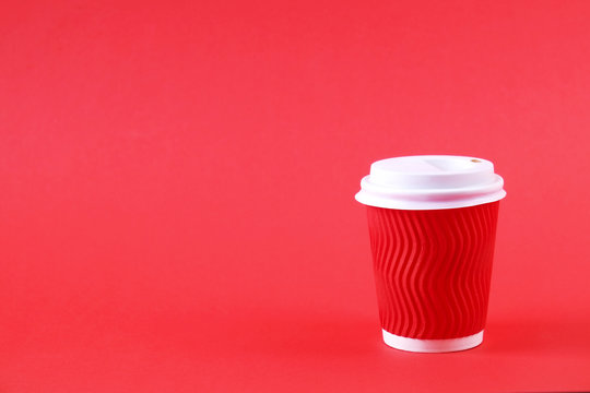 Brown disposable safe heat resistant double walled paper take out cup of coffee to go. Colorful eco-friendly cardboard mug for hot beverages, white cap on bright red background, close up copy space.