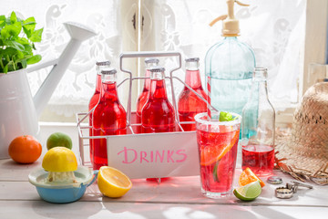 Red orangeade in bottle with citrus fruit on white table