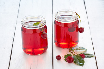 Homemade fresh cherry juice in a glass and fresh cherries on white wooden table
