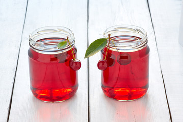 Homemade fresh cherry juice in a glass and fresh cherries on white wooden table
