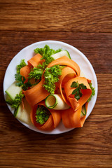 Artistically served vegetable salad with carrot, cucumber, letucce over wooden background, selective focus