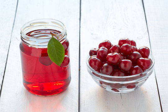 Homemade fresh cherry juice in a glass and fresh cherries on white wooden table