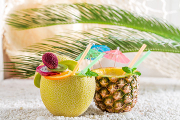 Tropical drinks in fresh fruits on white pebbles