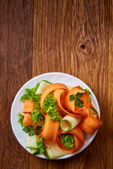 Artistically served vegetable salad with carrot, cucumber, letucce over wooden background, selective focus