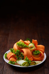 Artistically served vegetable salad with carrot, cucumber, letucce over wooden background, selective focus