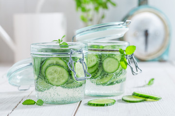 Refreshing water in jar with cucumber on white table