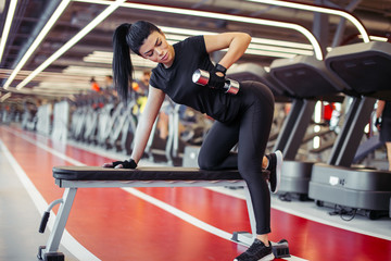 portrait of fit woman exercising one arm dumbbell row on bench for back muscles in gym