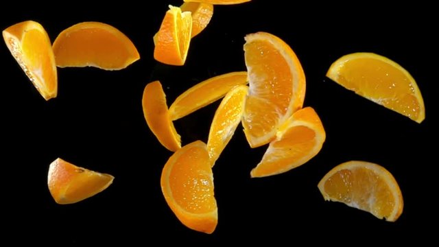 Slices of orange bouncing against to the camera on a black background in slow motion