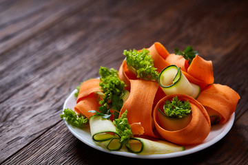 Fototapeta na wymiar Artistically served vegetable salad with carrot, cucumber, letucce over wooden background, selective focus