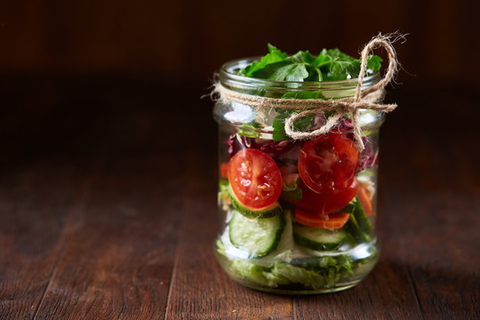 Creative vegetable salad served in glass jar over dark wooden background, selective focus, shallow depth of field