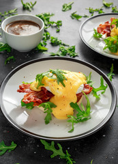 Eggs Benedict on english muffin with crispy bacon, wild rocket salad and hollandaise sauce.
