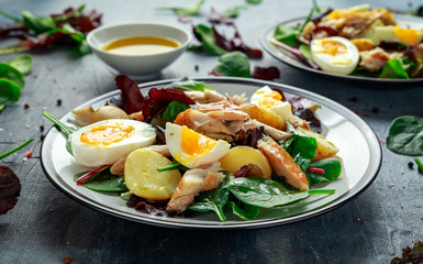 Warm Smoked Mackerel Salad with new potato, eggs, green lettuce mix in a plate.