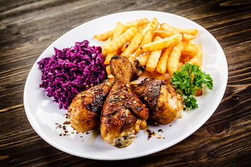 Grilled drumsticks with french fries and vegetables on wooden background