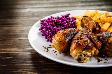 Grilled drumsticks with french fries and vegetables on wooden background