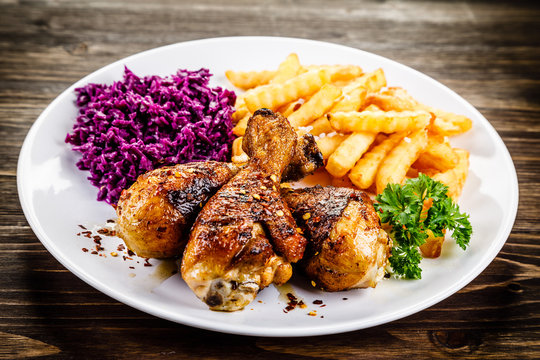 Grilled drumsticks with french fries and vegetables on wooden background